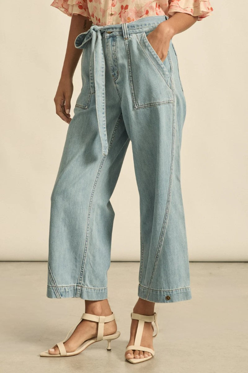 Person wearing light blue denim pants with a tie-waist and beige sandals on a neutral background
