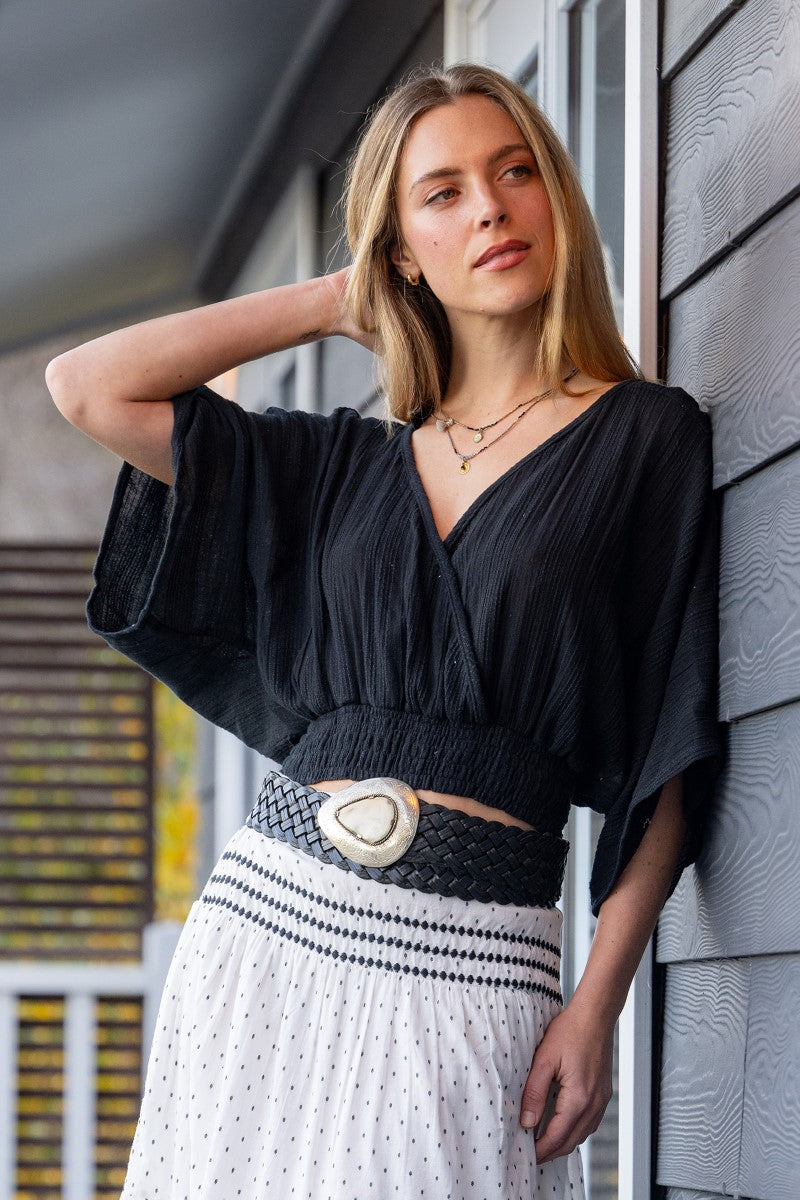 Woman in a black top and white skirt leaning against a building.