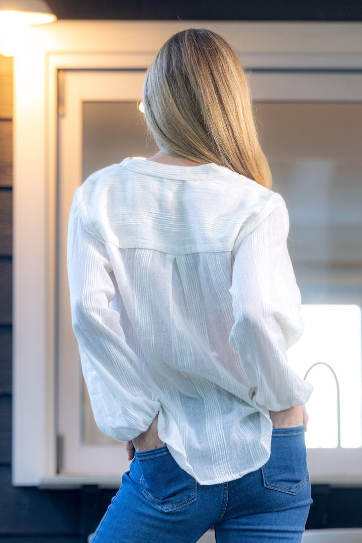 Person wearing a white blouse and blue jeans standing in front of a mirror.