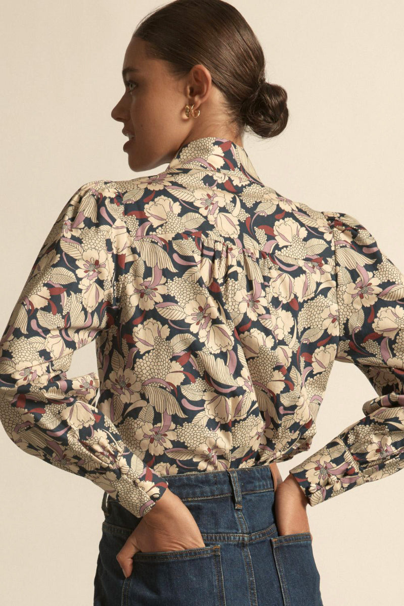 Woman wearing a long sleeve berry garden button down with blue jeans in beige background.