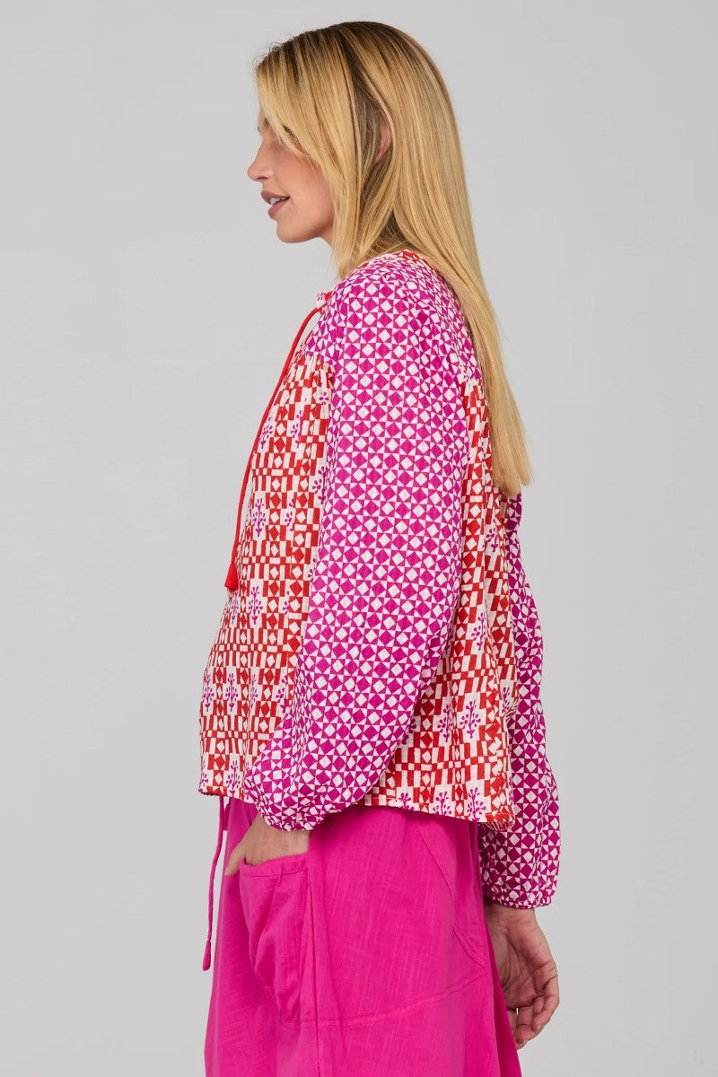 Woman wearing a pink and red patterned top with a plain background