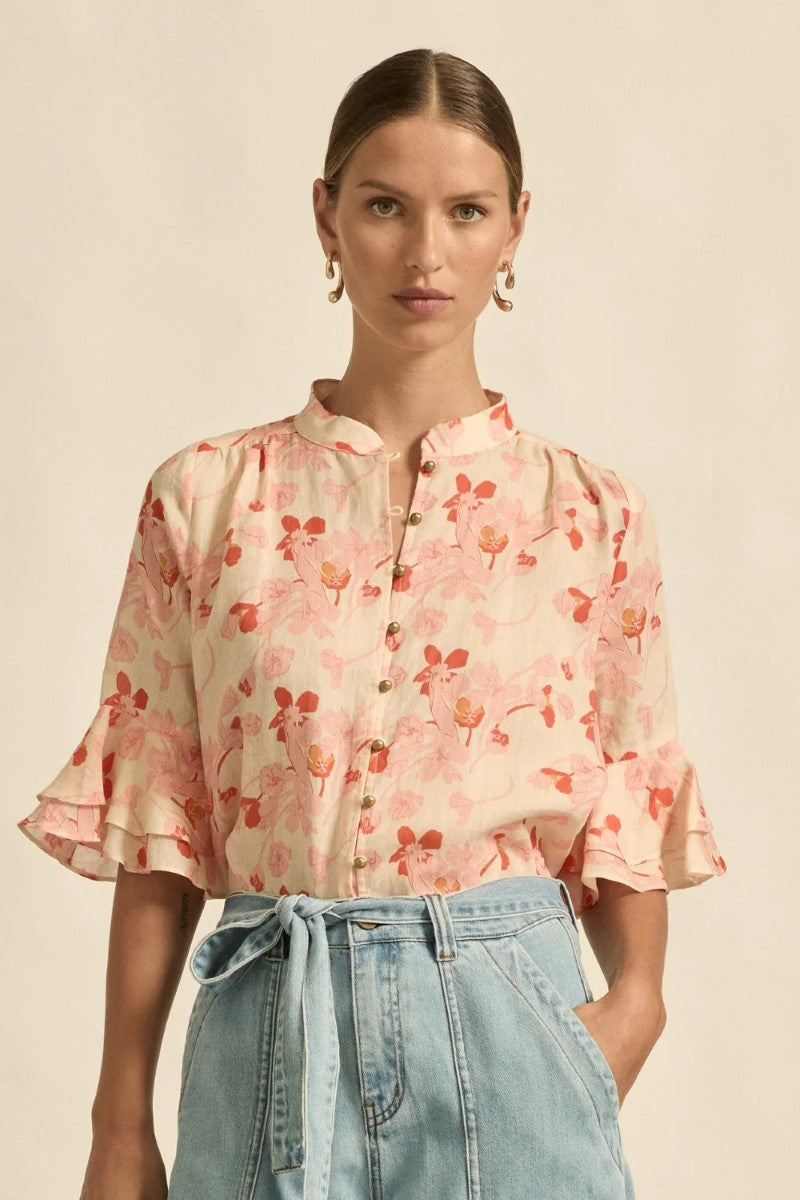 Woman wearing a floral blouse with ruffled sleeves against a beige background