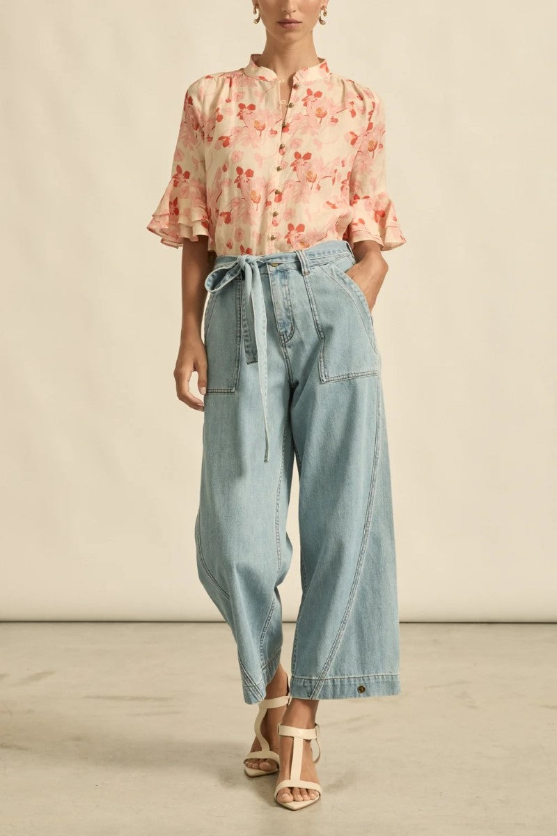 Person wearing a floral blouse and light blue jeans on a neutral background