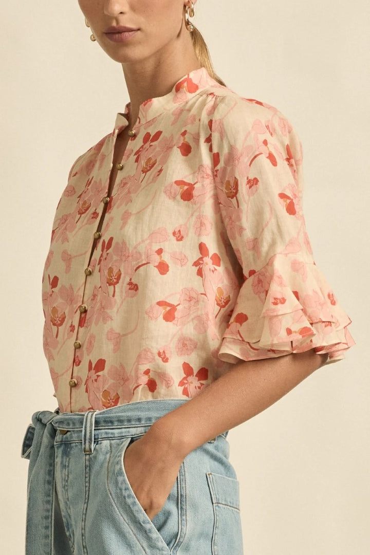 Woman wearing a floral blouse with rolled-up sleeves and light blue jeans on a beige background