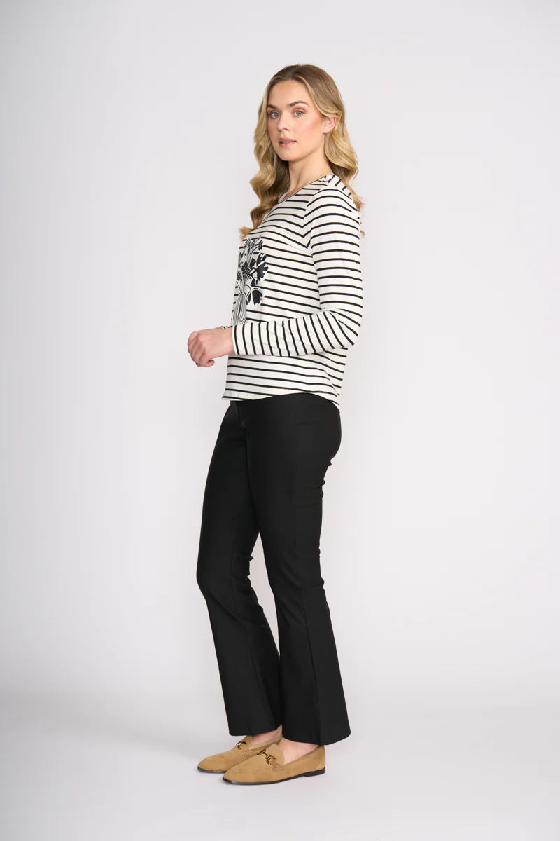 Woman wearing a black and white striped top with a graphic design and black pants on a white background