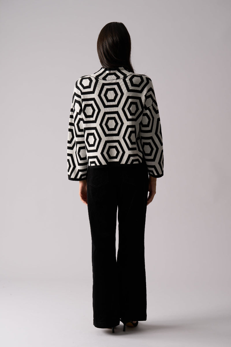 Person wearing a black and white geometric patterned blouse with black pants on a light gray background