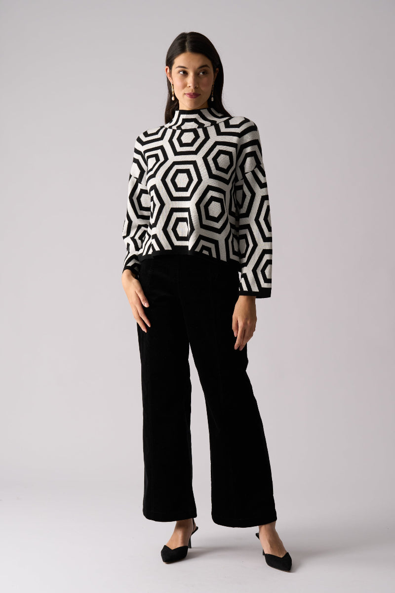 Woman wearing a black and white geometric patterned sweater with black pants on a light gray background