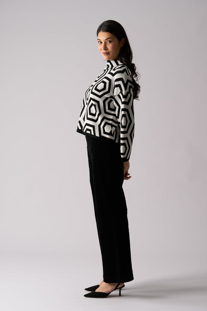 Woman wearing a black and white geometric patterned top with black pants on a light gray background