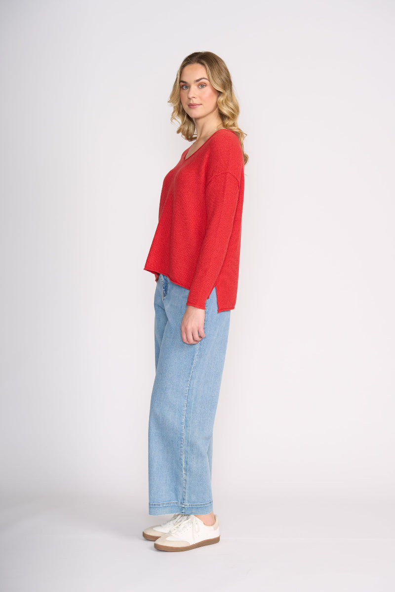 Woman wearing a red sweater and blue jeans on a white background