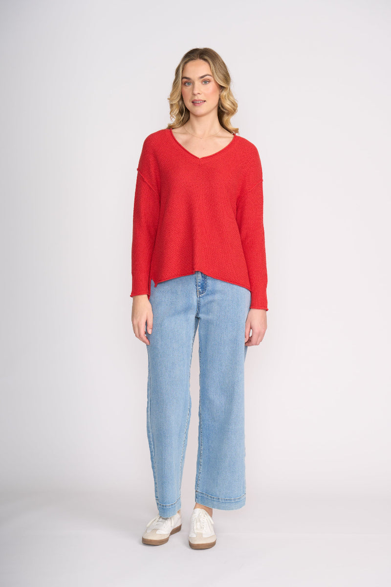Woman wearing a red sweater and light blue jeans on a white background