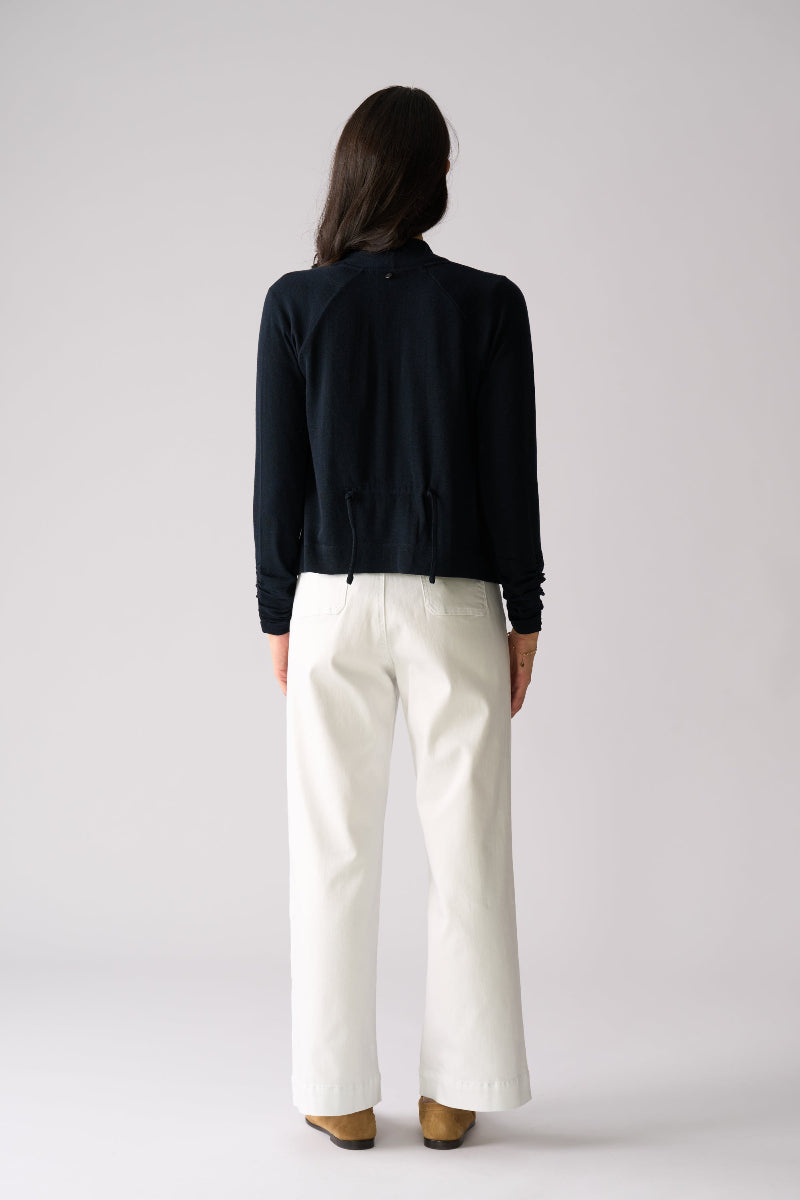 Person wearing a black jacket and white pants on a plain background