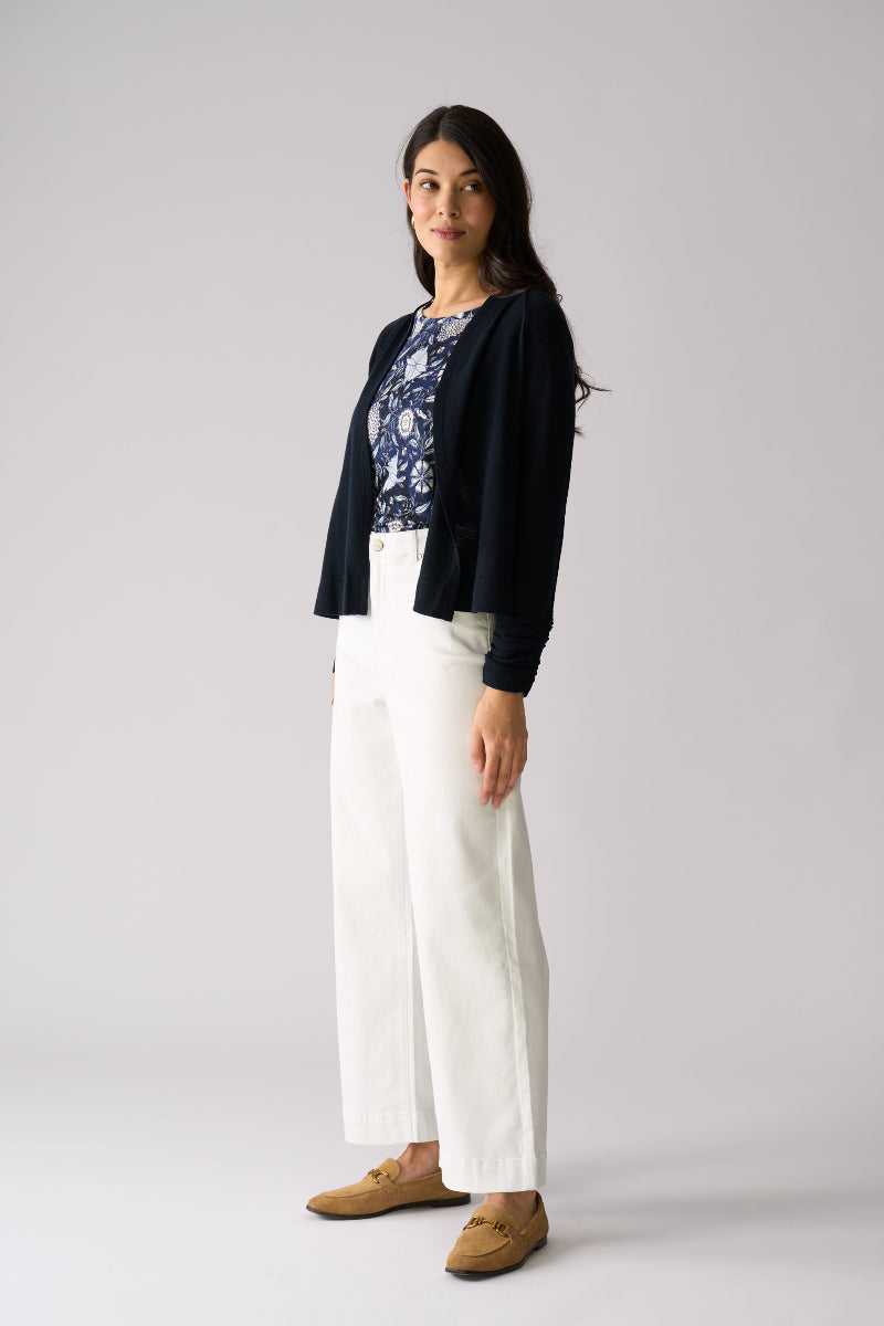 Woman wearing a black cardigan, floral top, white pants, and brown shoes on a gray background