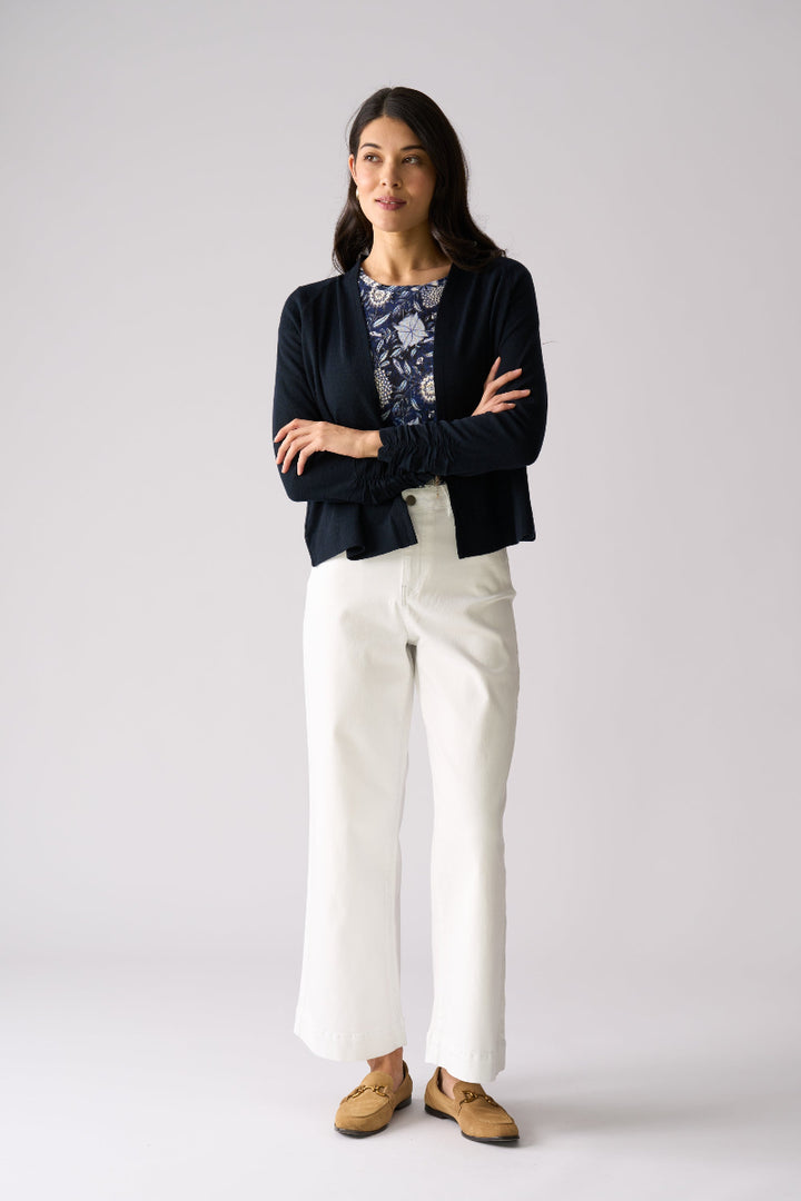 Woman wearing a black cardigan, floral top, white pants, and brown shoes on a gray background