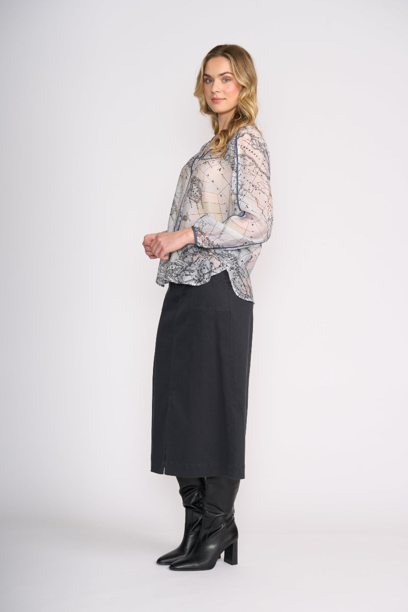 Woman wearing a patterned blouse, black skirt, and black boots on a white background
