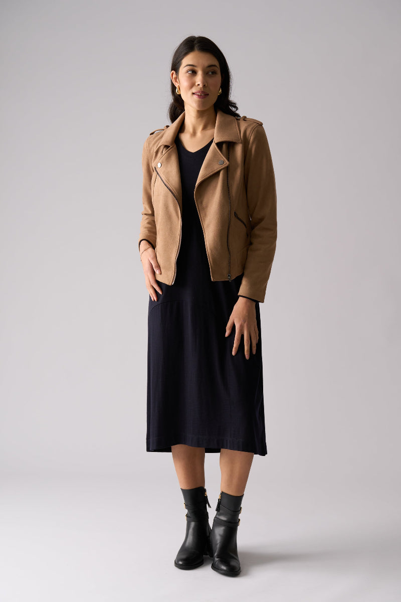 Woman wearing a tan jacket over a black dress on a white background
