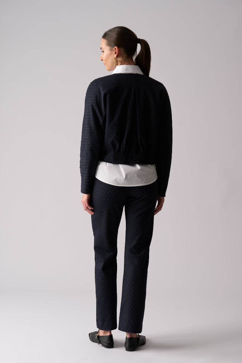 Woman wearing a black cardigan, white blouse, and black pants on a gray background