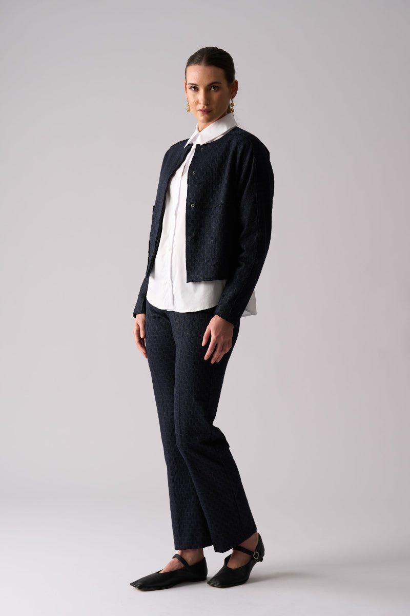 Woman wearing a black cardigan, white blouse, and black pants on a gray background