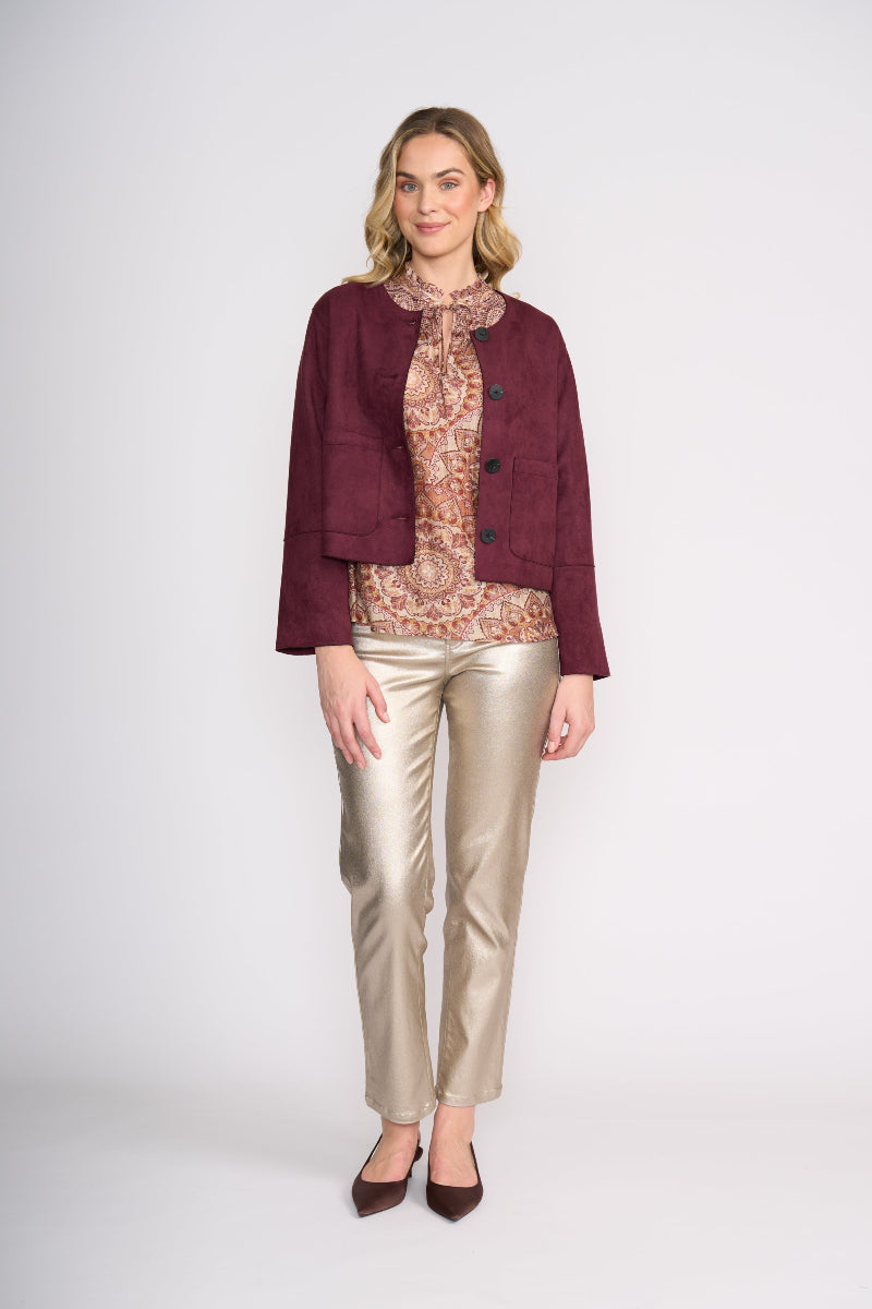 Woman wearing a burgundy jacket, patterned blouse, and gold pants on a white background