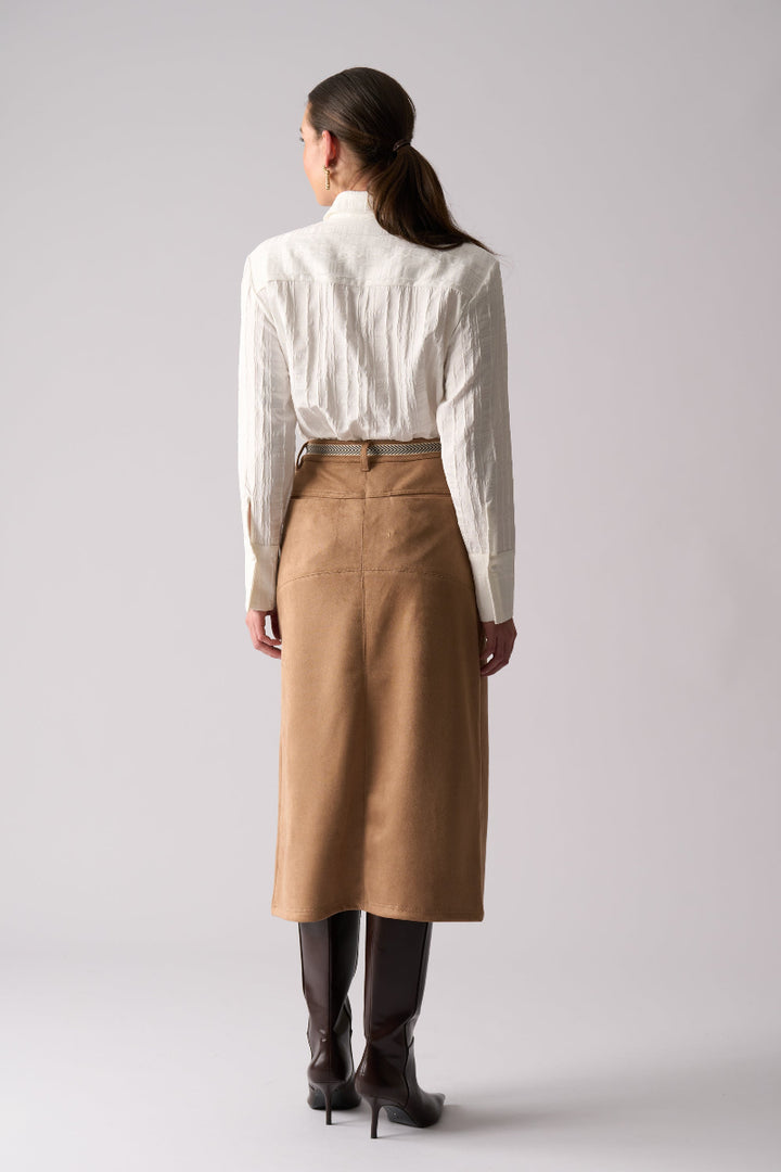 Woman wearing a white blouse and tan skirt on a plain background