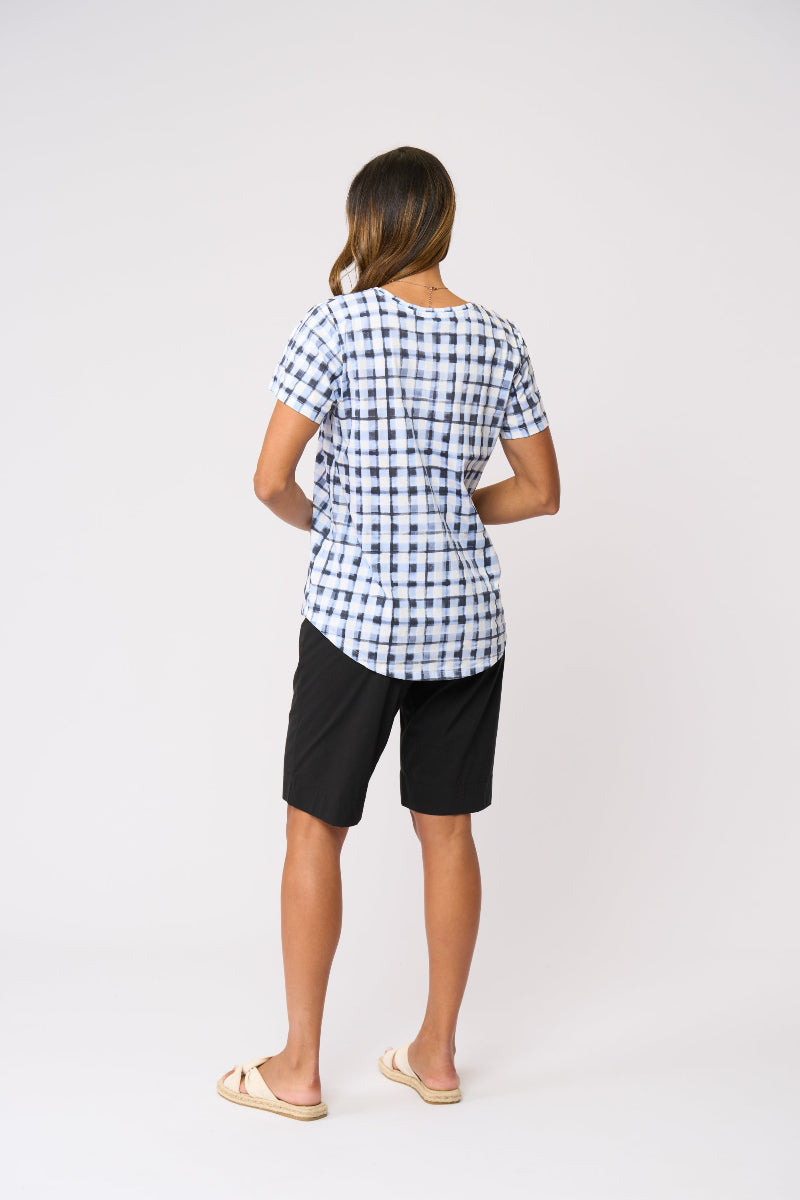 A woman shown from the back wearing a short-sleeve blue and white gingham check t-shirt, black shorts, and beige slide sandals, standing against a plain white studio background.