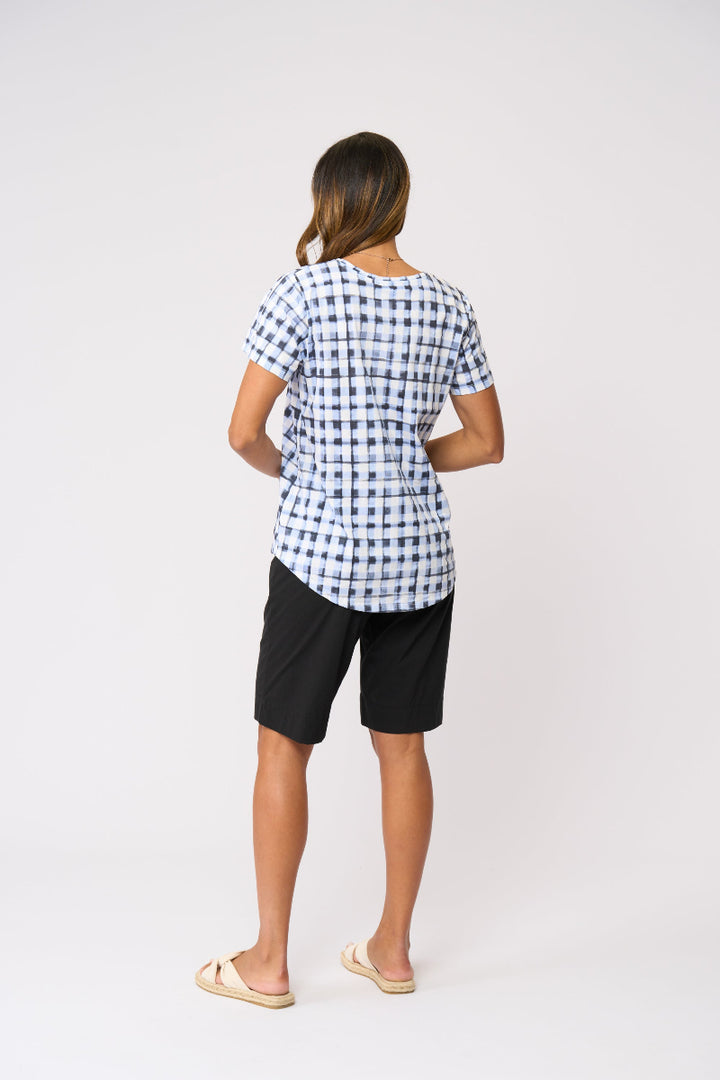 A woman shown from the back wearing a short-sleeve blue and white gingham check t-shirt, black shorts, and beige slide sandals, standing against a plain white studio background.