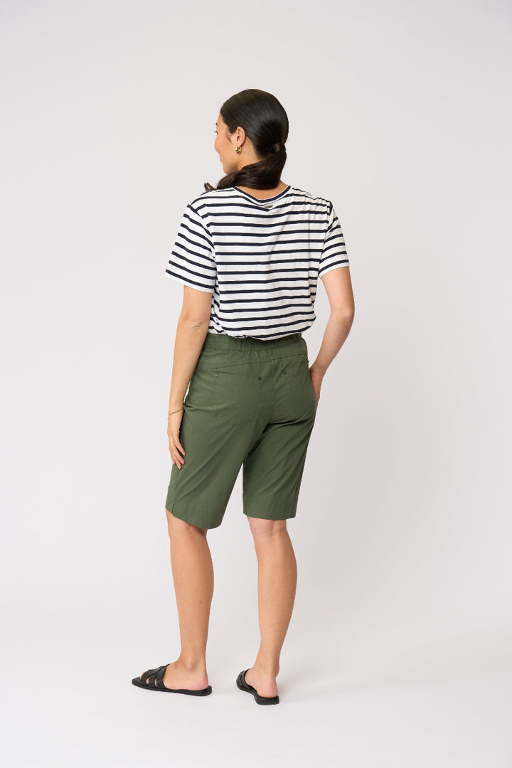 A woman is shown from the back wearing a black and white horizontally striped short-sleeve t-shirt, olive green shorts, and black slide sandals, set against a plain light gray studio background.