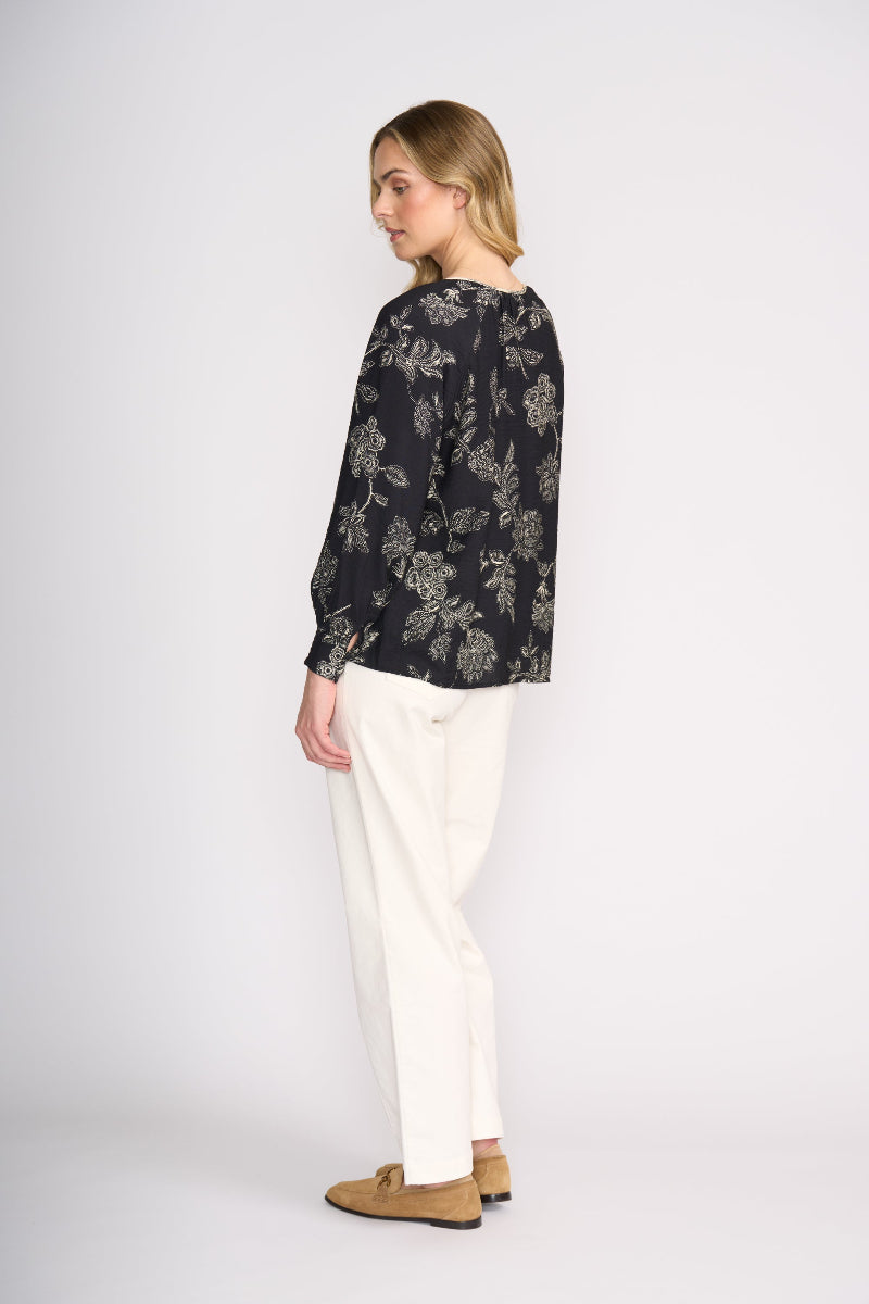 Woman wearing a black floral blouse and white pants on a white background