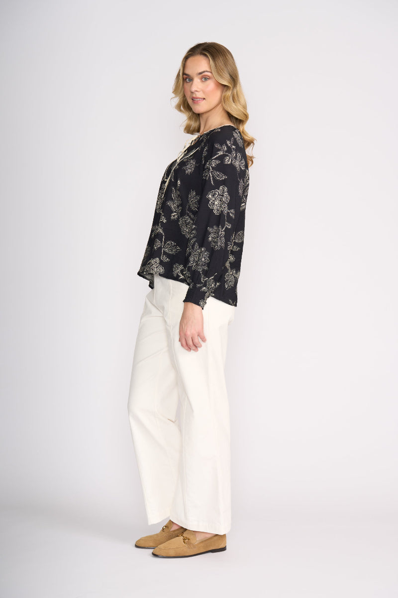 Woman wearing a black floral blouse and white pants on a white background