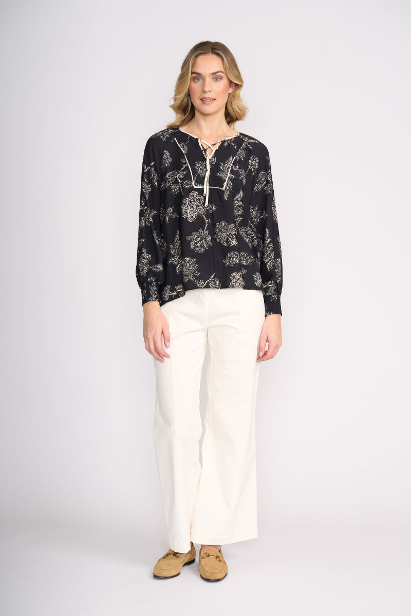 Woman wearing a black floral blouse and white pants on a white background