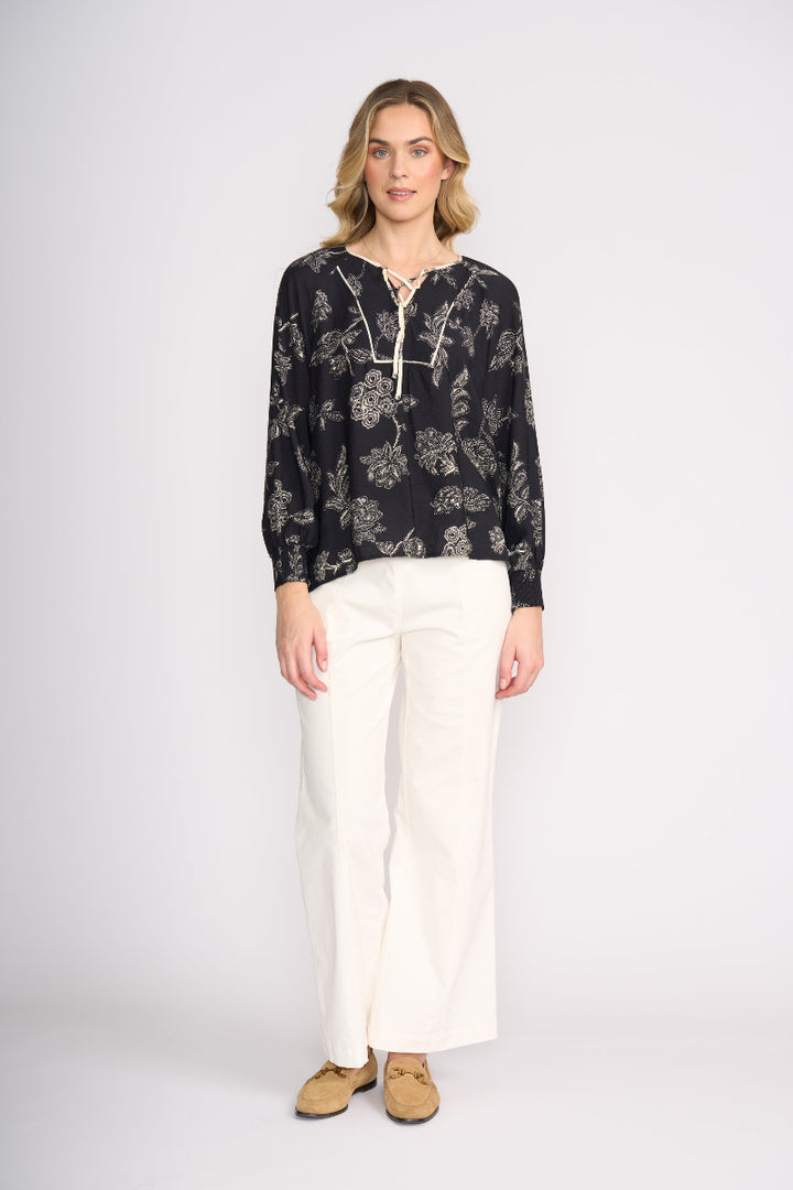 Woman wearing a black floral blouse and white pants on a white background