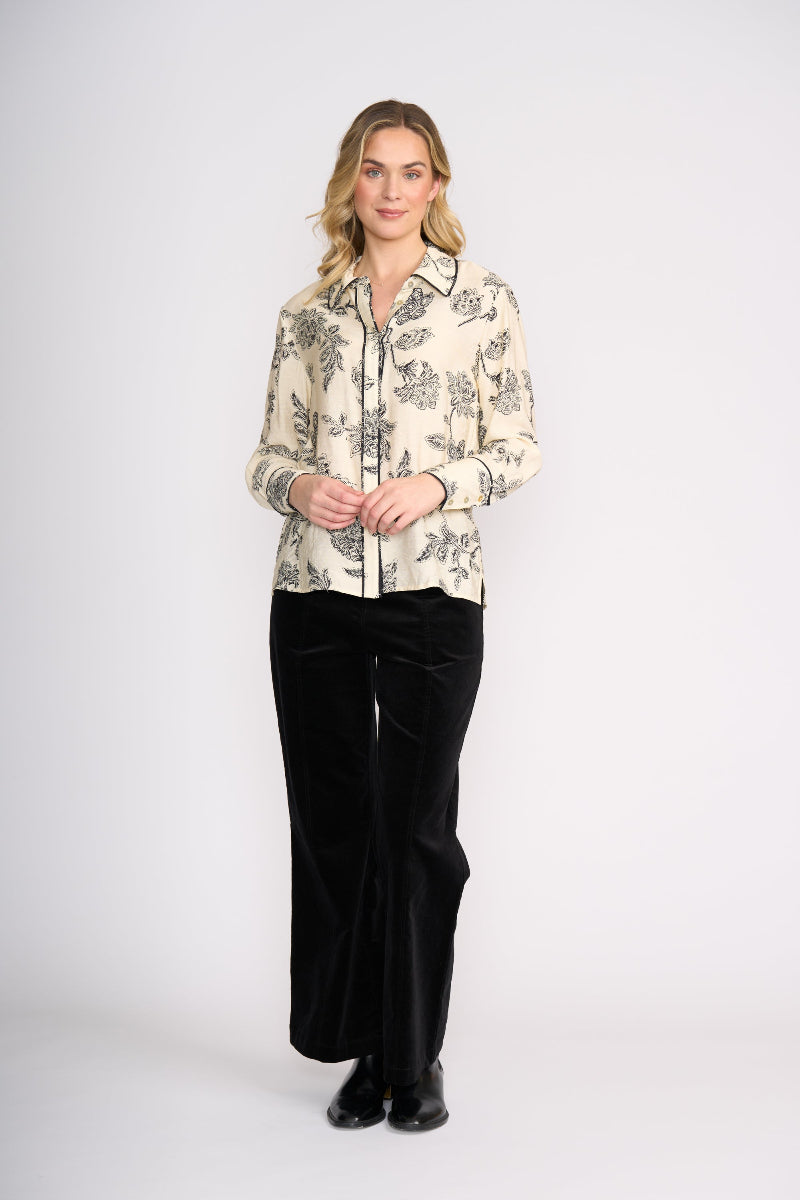 Woman wearing a patterned blouse and black pants on a white background