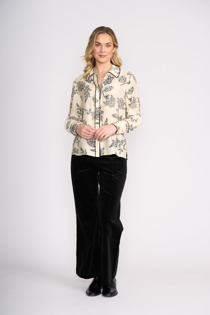 Woman wearing a patterned blouse and black pants on a white background
