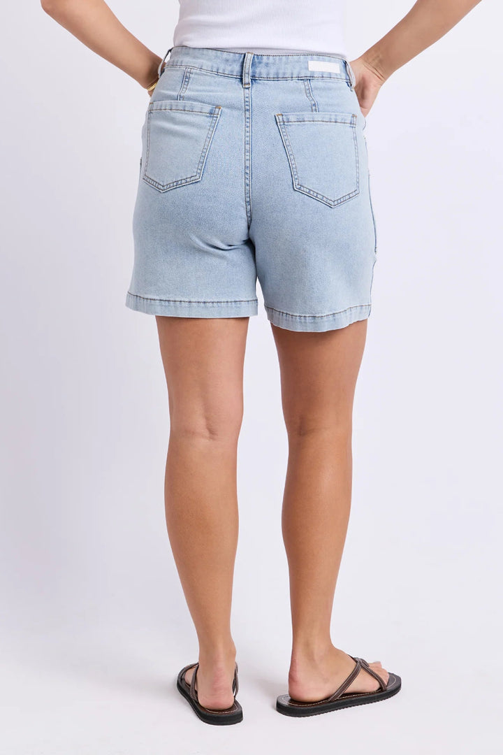 A person shown from the back wearing light-wash denim shorts, a white top, and black sandals against a plain light gray studio background.