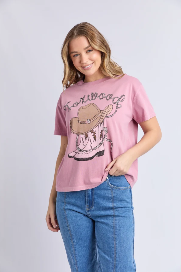 Woman wearing a pink t-shirt with a cowboy hat graphic and blue jeans on a light gray background