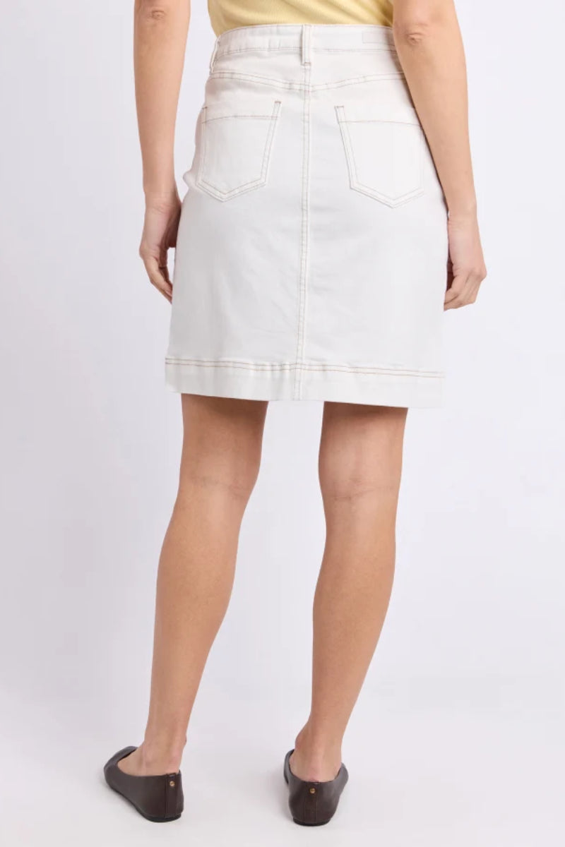 A model from the back wearing a light off-white denim mini skirt with back patch pockets, paired with a yellow top and dark brown flats, against a plain light gray studio background.