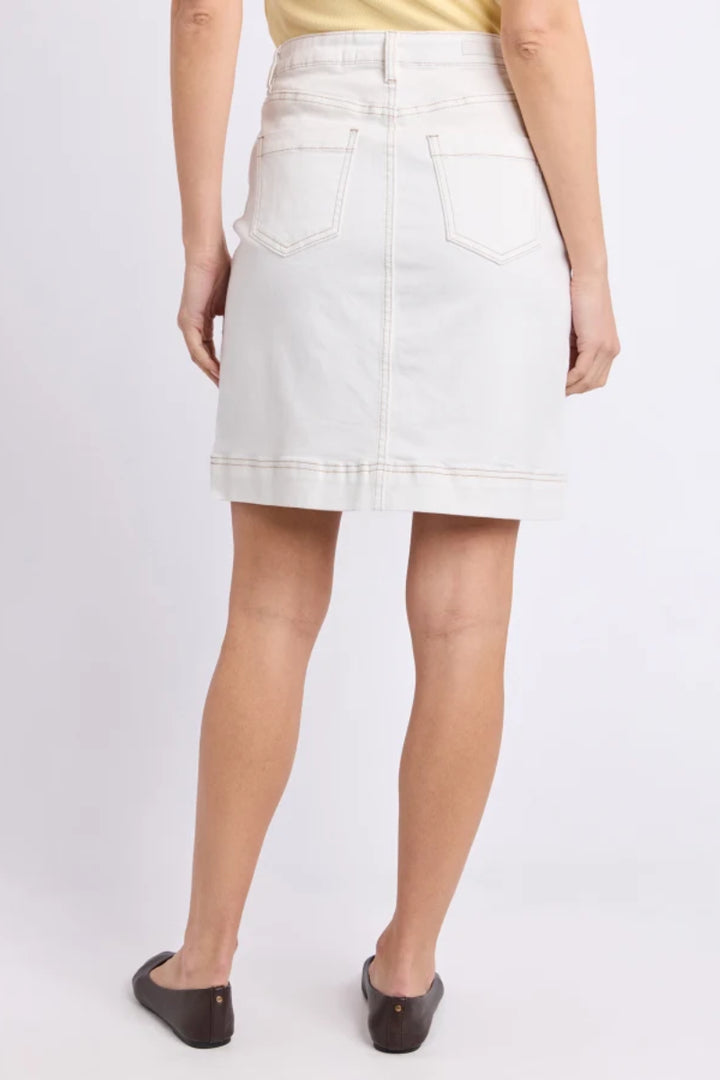 A model from the back wearing a light off-white denim mini skirt with back patch pockets, paired with a yellow top and dark brown flats, against a plain light gray studio background.