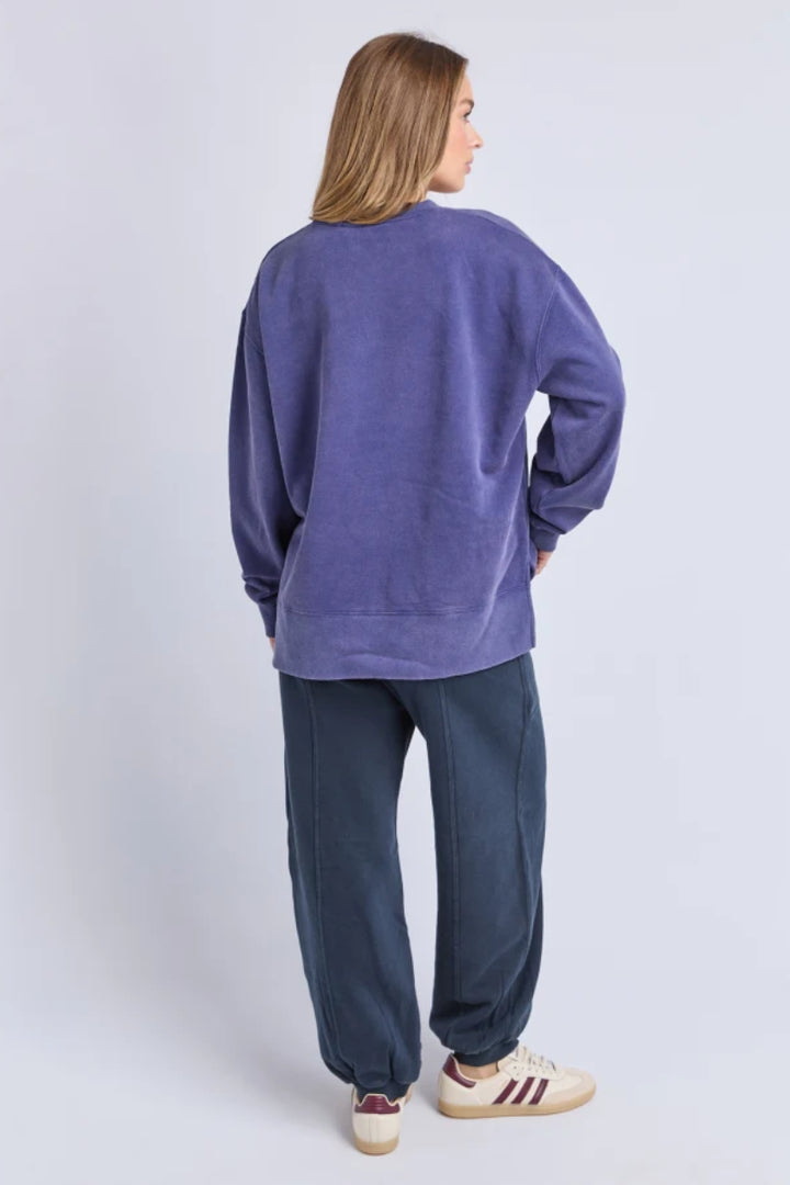 Person wearing a purple sweatshirt and dark pants on a light gray background