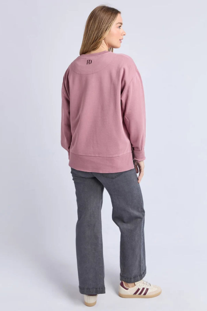 Person wearing a pink sweatshirt with a logo on the back, standing against a light purple background.