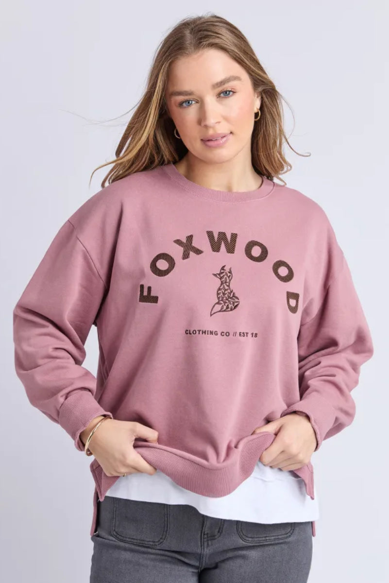 Woman wearing a pink sweatshirt with 'FOXWOOD' branding on a light gray background