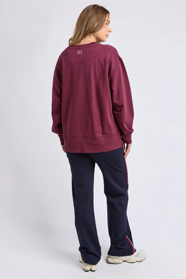 Person wearing a maroon sweatshirt and navy pants on a white background