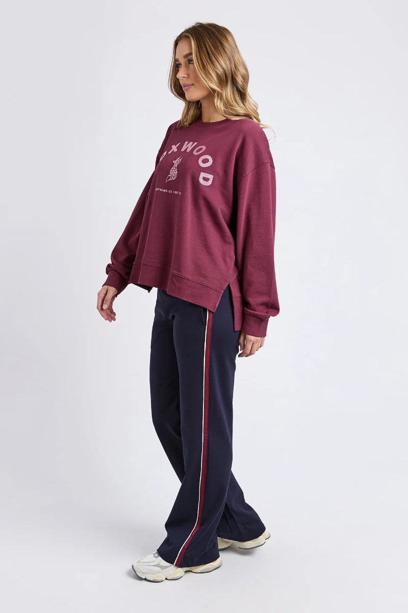 Woman wearing a maroon sweatshirt and navy tracksuit with red stripes on a white background