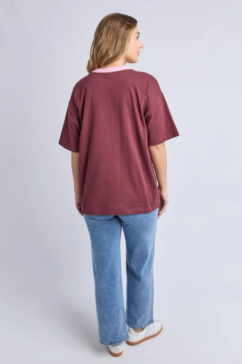 Woman wearing a maroon oversized t-shirt and blue jeans on a light gray background