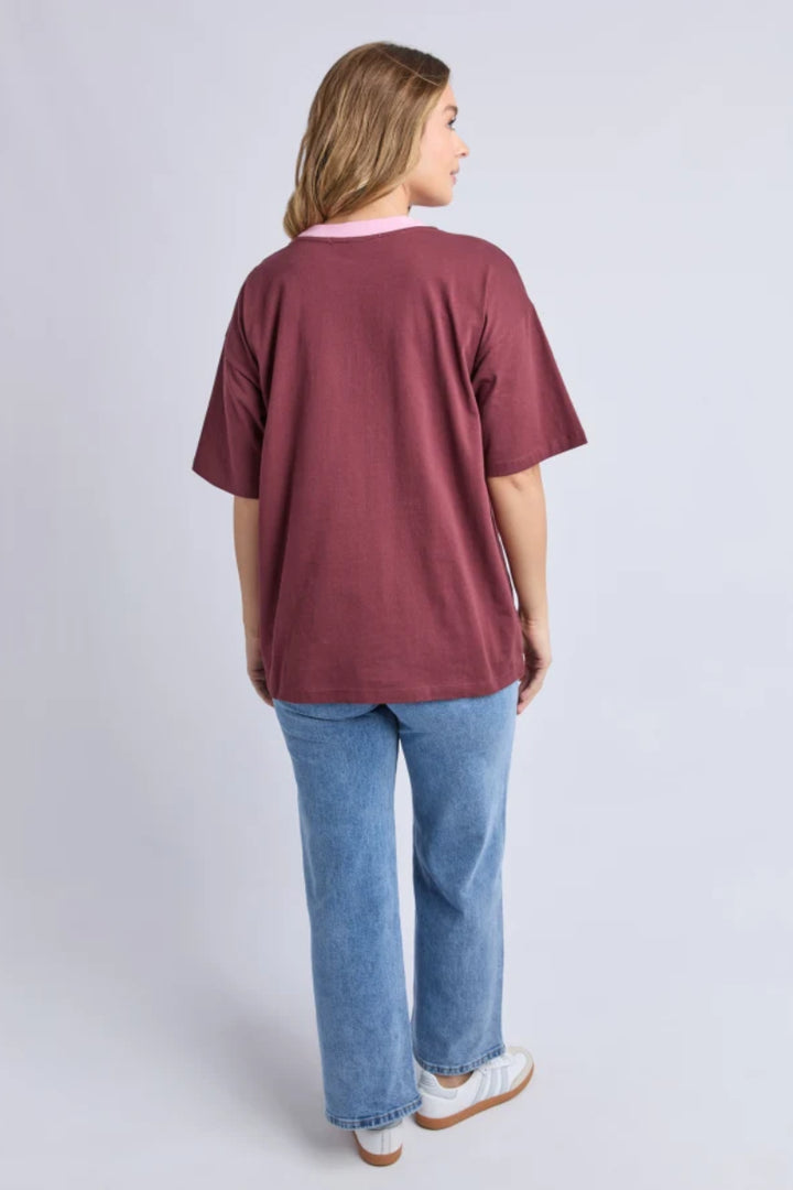 Woman wearing a maroon oversized t-shirt and blue jeans on a light gray background