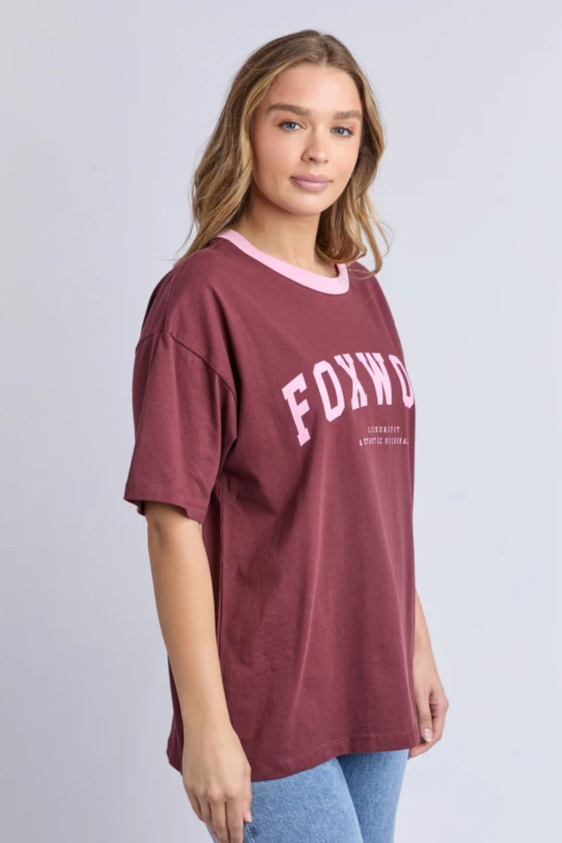 Woman wearing a maroon t-shirt with 'FOXWOOD' printed on it against a plain background
