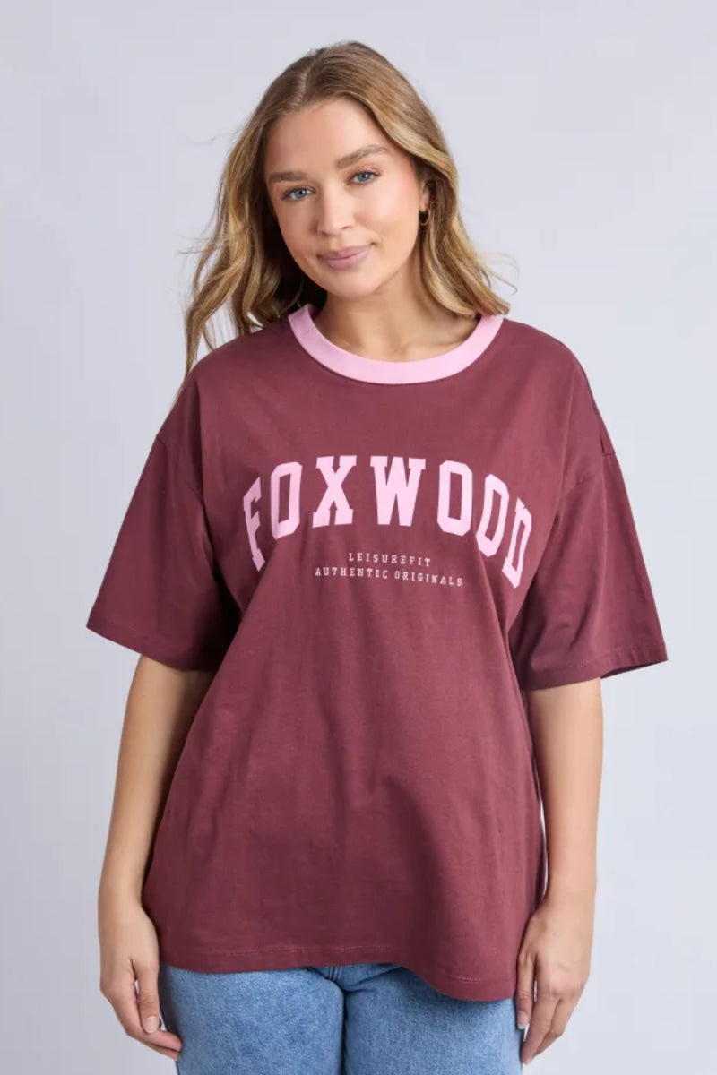 Woman wearing a maroon t-shirt with 'FOXWOOD' printed on it against a plain background