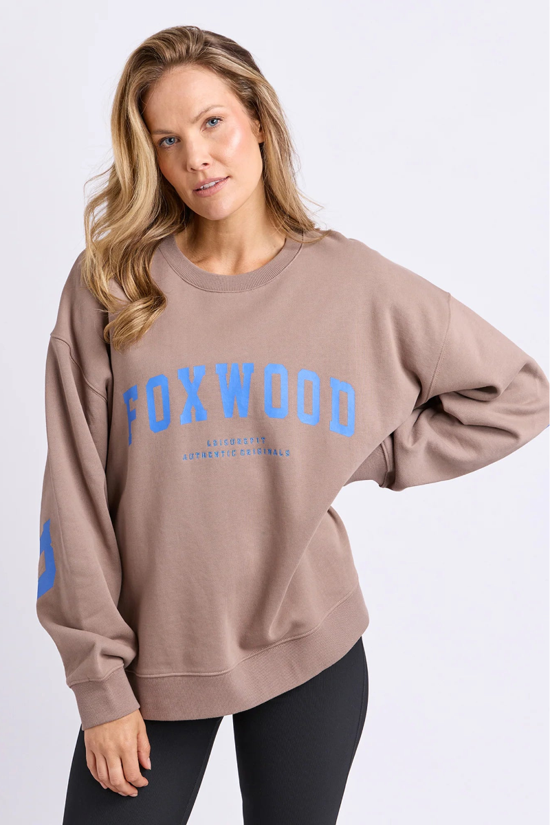 Woman wearing a beige sweatshirt with 'FOXWOOD' printed in blue on a white background