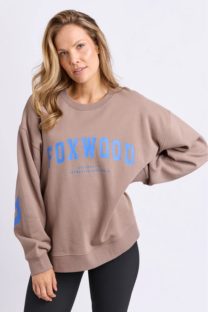 Woman wearing a beige sweatshirt with 'FOXWOOD' printed in blue on a white background