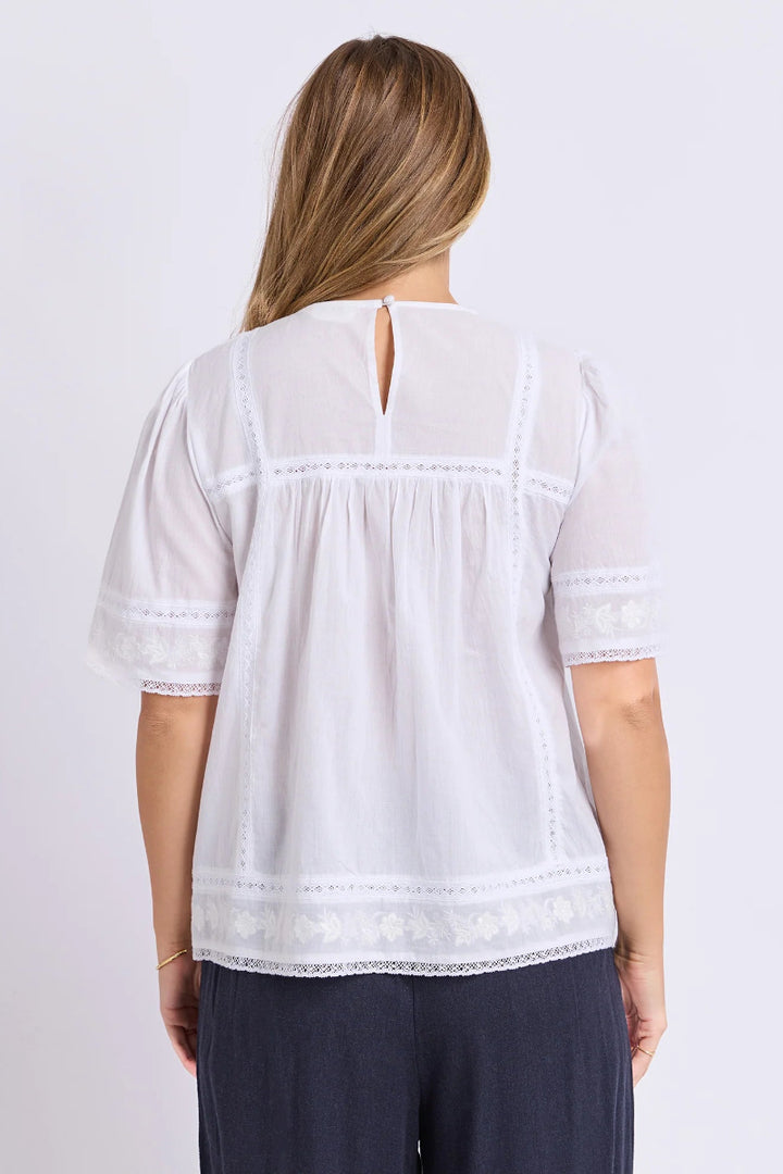 Woman wearing a white blouse with lace details on a plain background