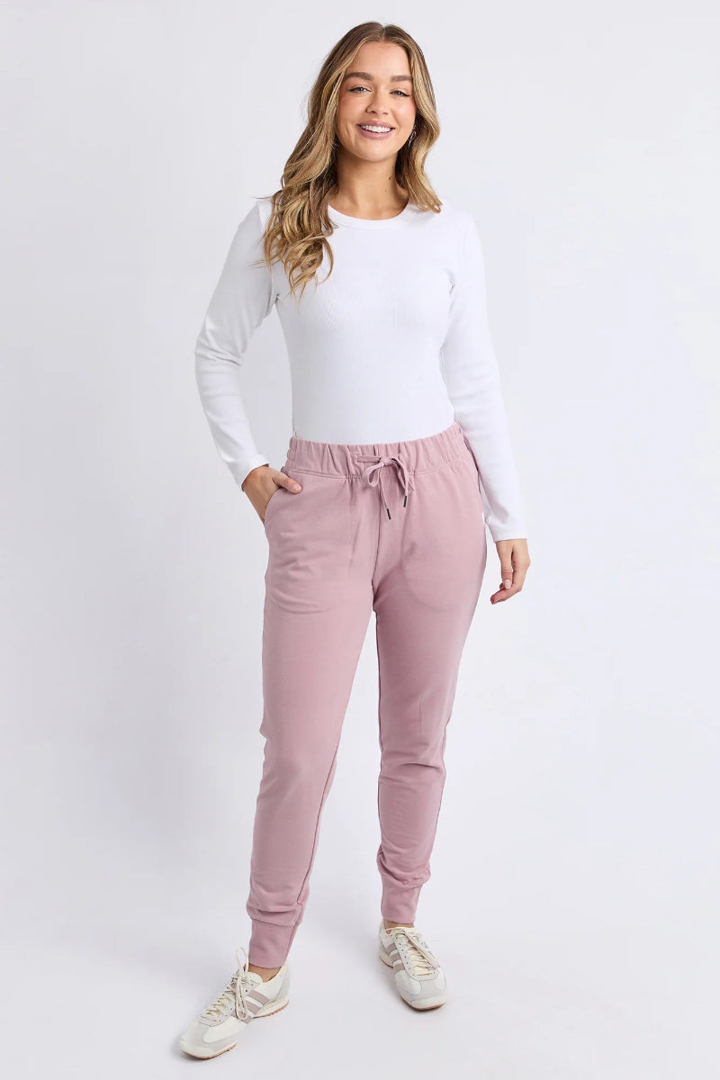 Woman wearing a white long-sleeve top and pink jogger pants on a white background