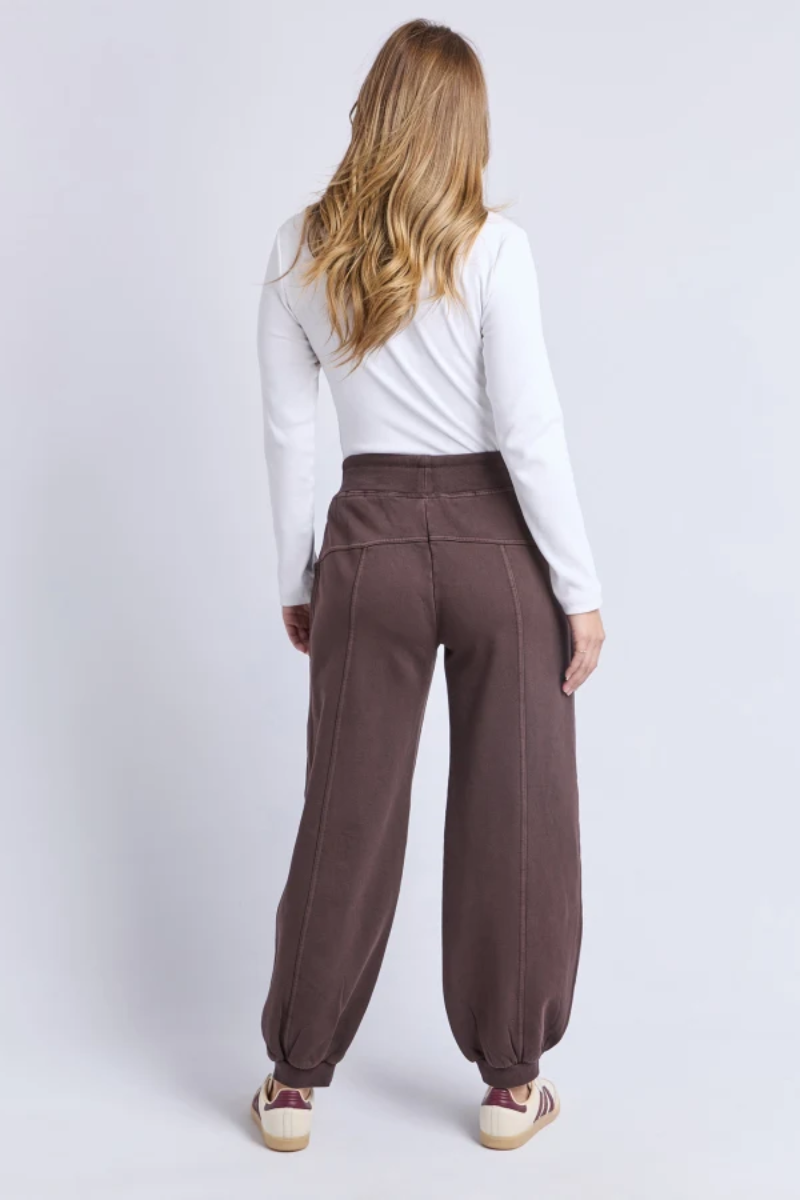Person wearing brown pants and a white top on a light gray background